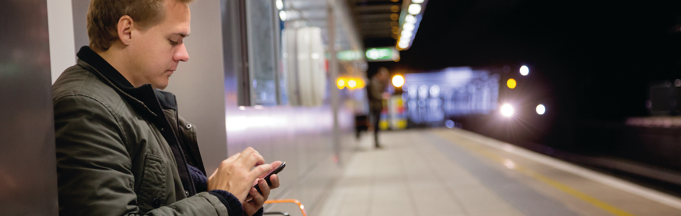 A man sitting on a railway platform looking at his smartphone